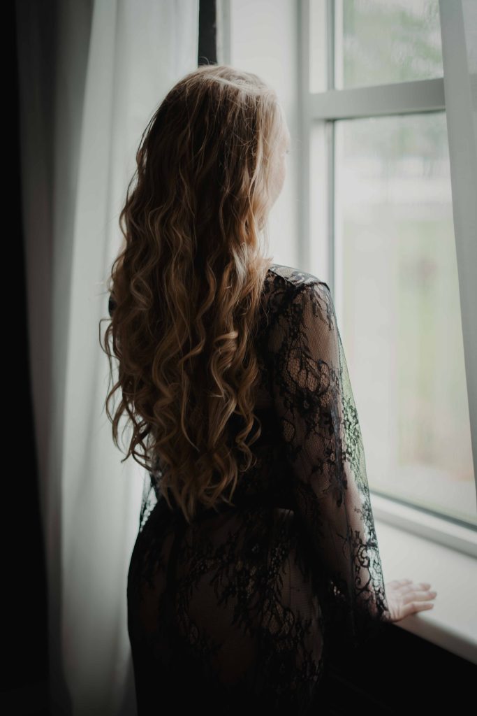 Vrouw in zwarte lingerie bij het raam tijdens een boudoir fotoshoot
