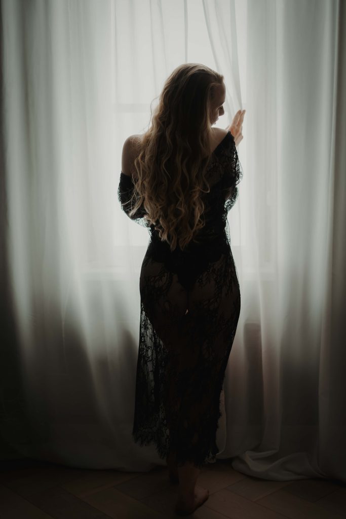 Vrouw met lang haar bij een raam tijdens een sfeervolle boudoir fotoshoot
